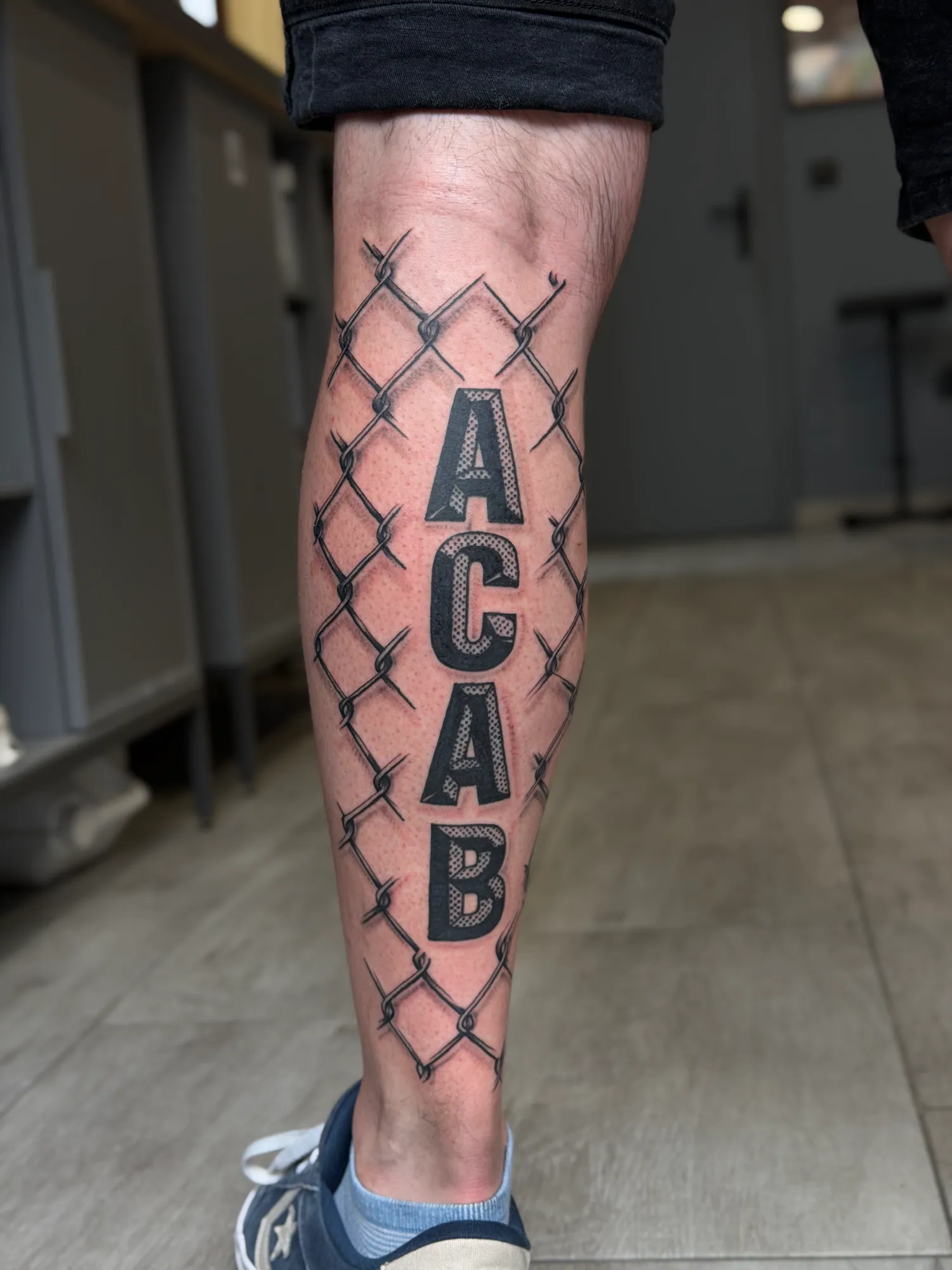 Lettering ACAB na łydce — Nastia Czarny tatuaż lettering ACAB z motywem metalowego ogrodzenia na łydce