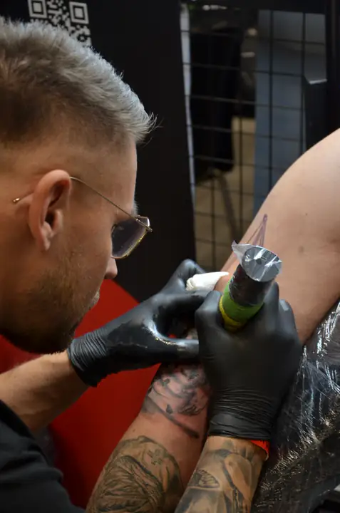 Tatuator wykonuje projekt w czerni i szarości na ramieniu