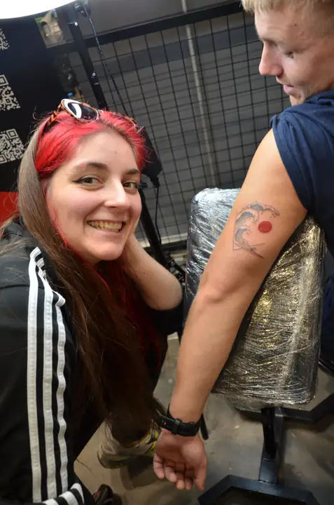 Uśmiechnięta tatuatorka prezentuje ukończony tatuaż z modelem